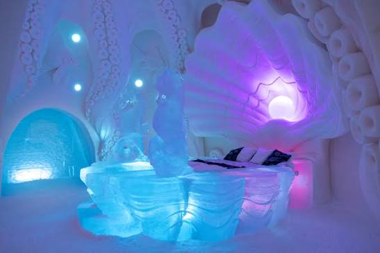 Vaulted snow hall with carved wall panels lit from behind in pale blue