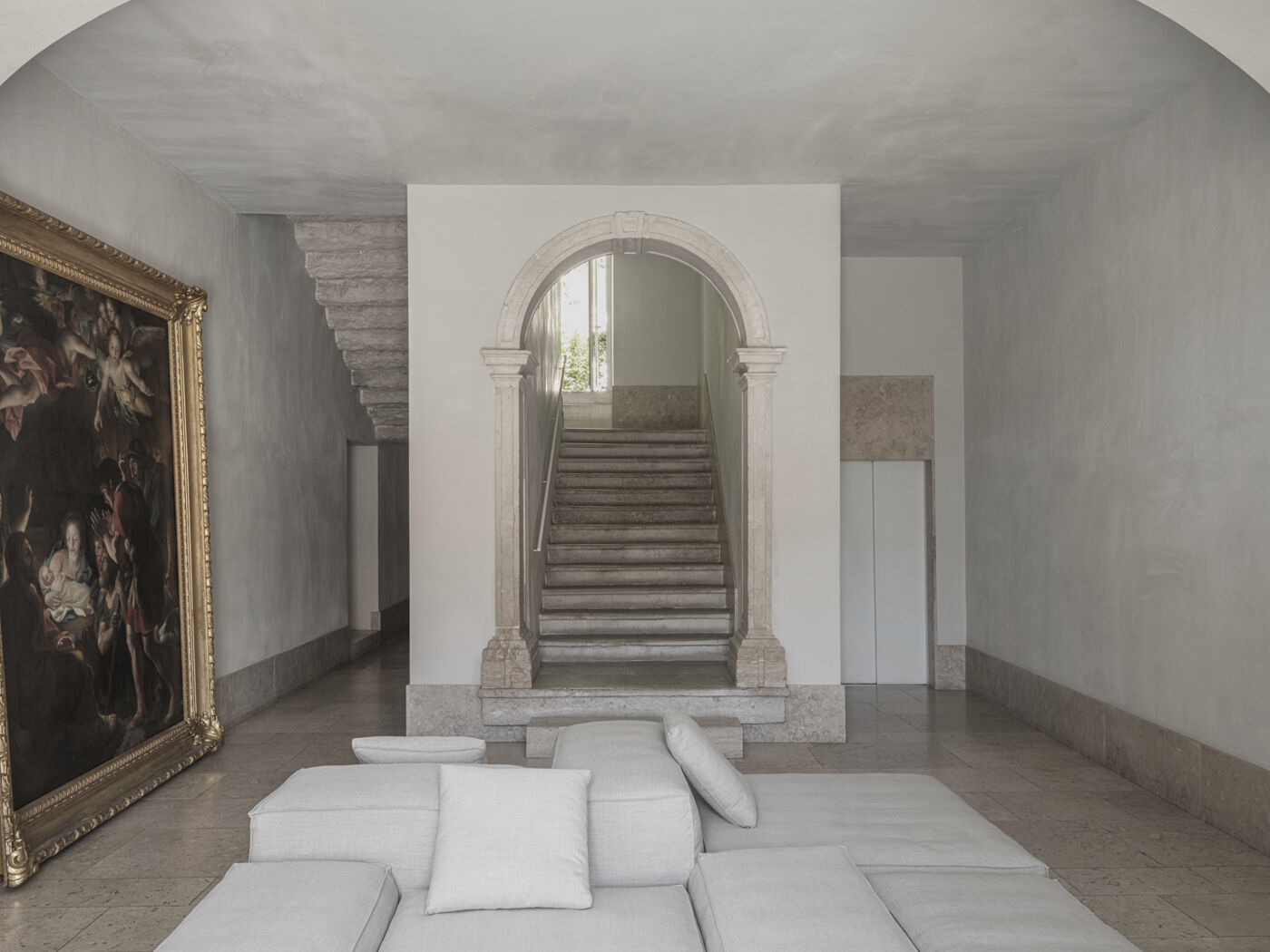 Pale stone stair rising against a plain rendered wall lit from a high window